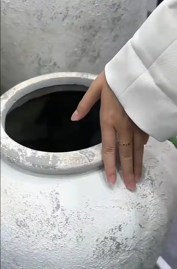 Hand examining the textured surface of a white round GRC planter